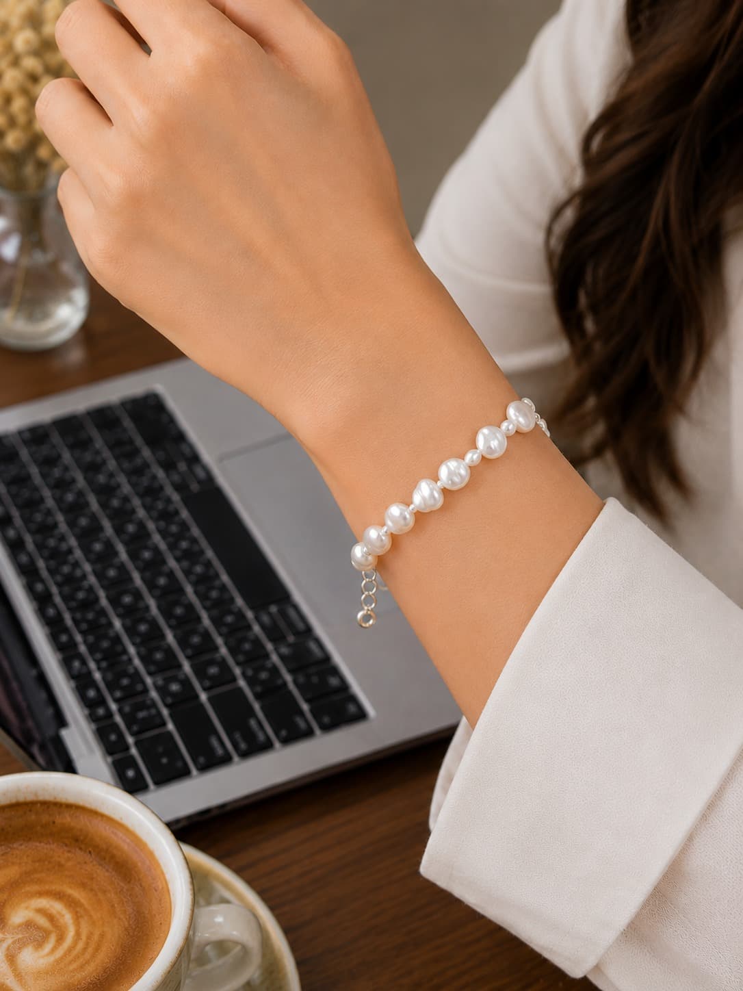 Pearl bracelet on a wrist beside a laptop and coffee — workwear